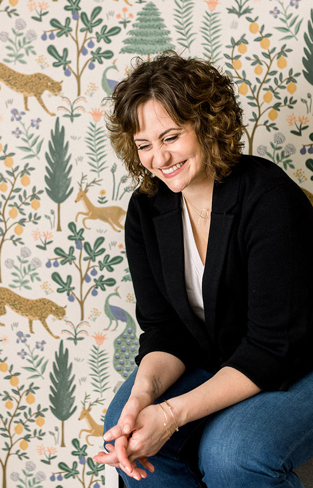 Paige sits against a backdrop of vibrant wallpaper featuring trees and woodland creatures.
