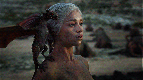 Daenarys Targaryen stares off into the distance, body covered in ash, with a baby dragon screeching on her shoulder.